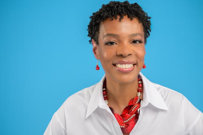 A picture of Shatanese smiling in a white shirt with a red scarf against a blue background. 