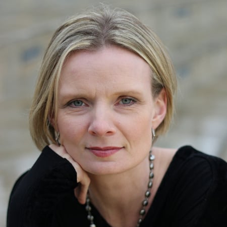 A picture of Jen with short blonde hair, wearing a black shirt and a necklace.