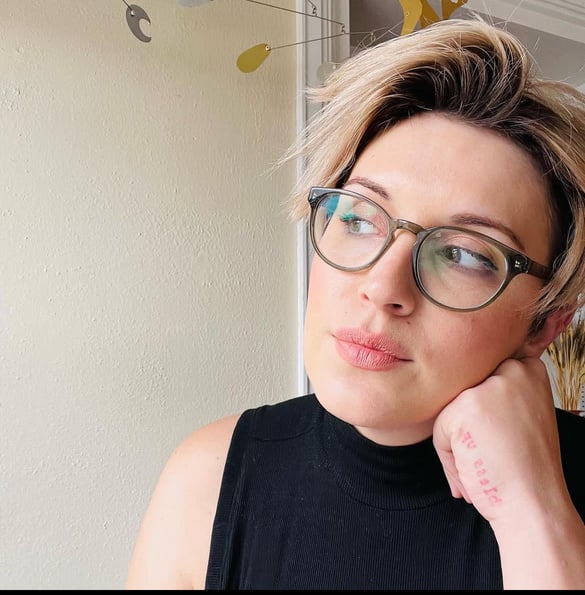 A picture of Cecil resting her head on her hand and looking to the side, wearing glasses and a black top.